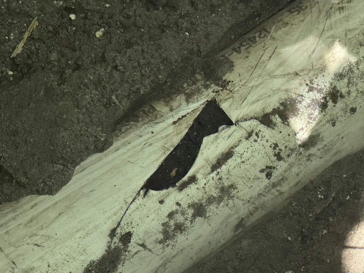 Cracked PVC sewer pipe with a broken-out hole, exposed in sandy soil in Neptune Beach, FL